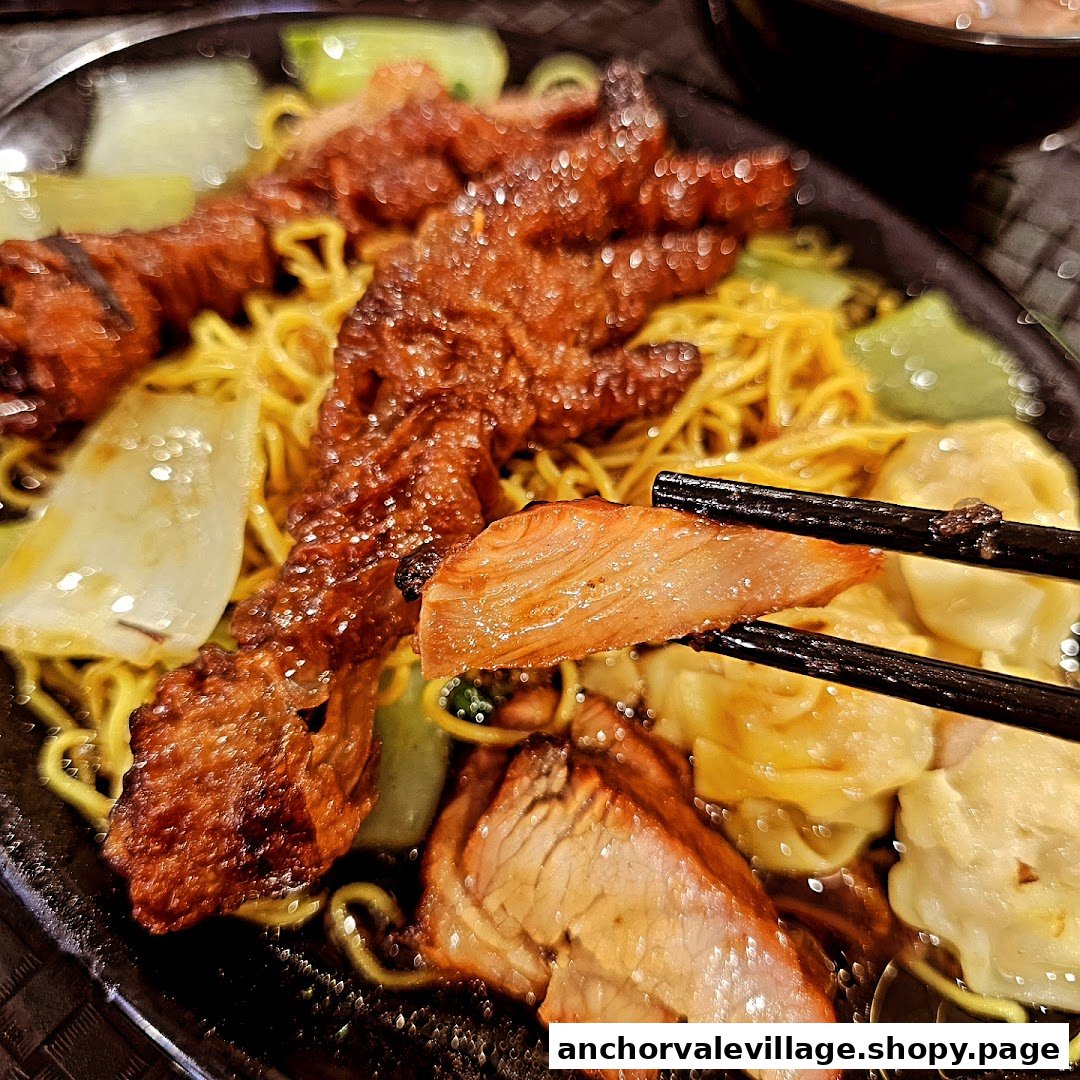 A close-up of roasted chicken feet, char siu, and wontons with noodles, held by chopsticks.