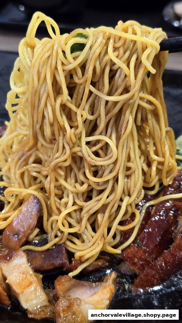 Close-up of delicious roasted meat noodles being lifted with chopsticks.
