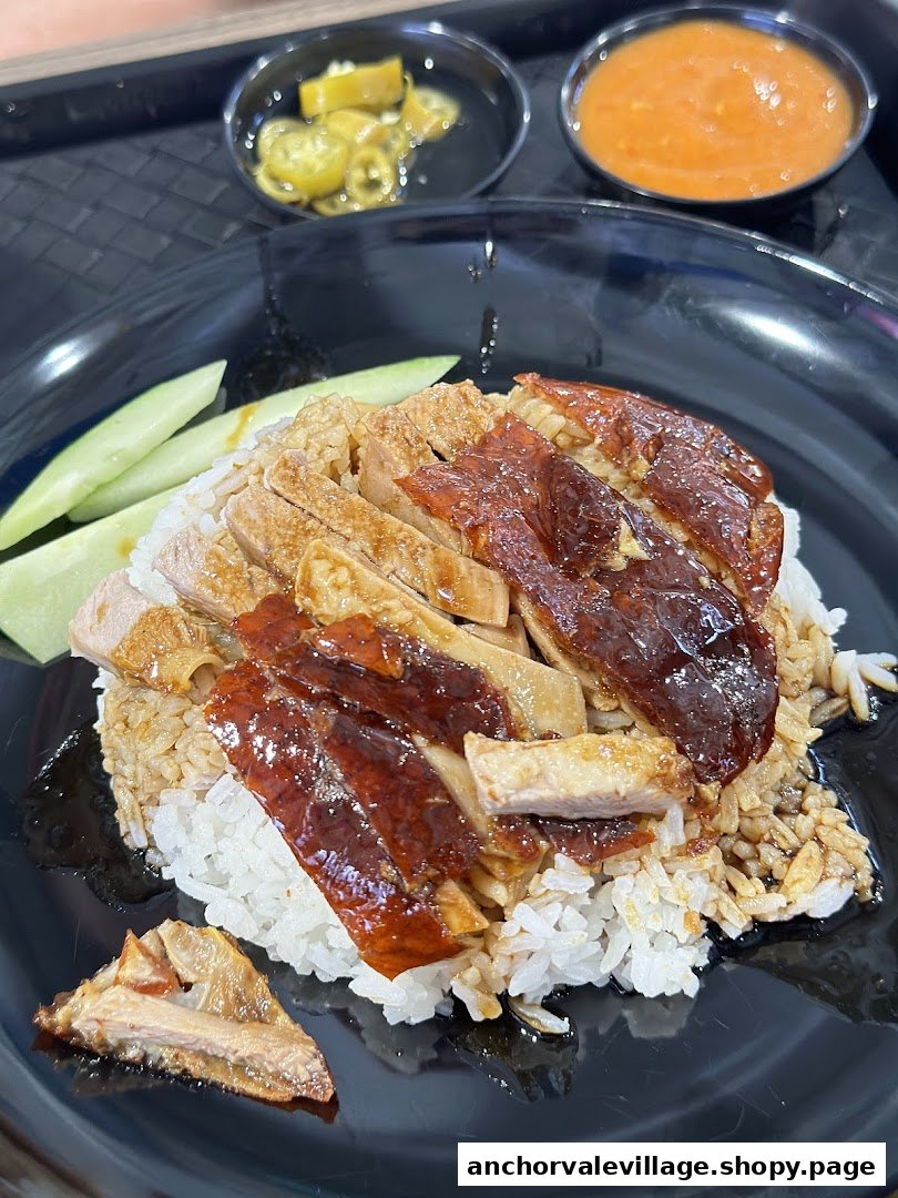 A plate of roasted duck and chicken on rice with cucumber slices and side sauces.
