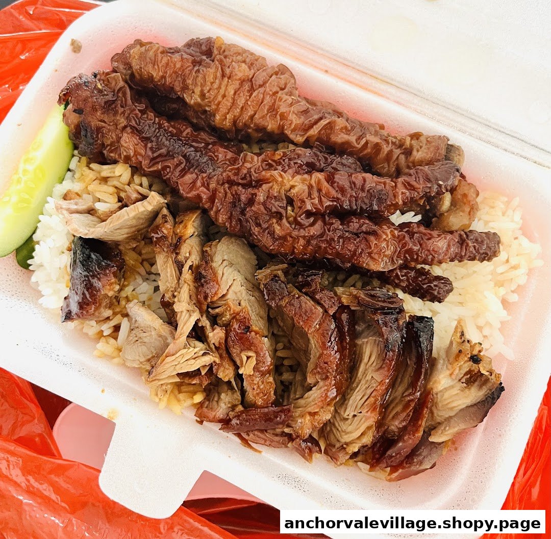 A takeaway box with roasted duck, crispy pork belly, and rice, served with cucumber.