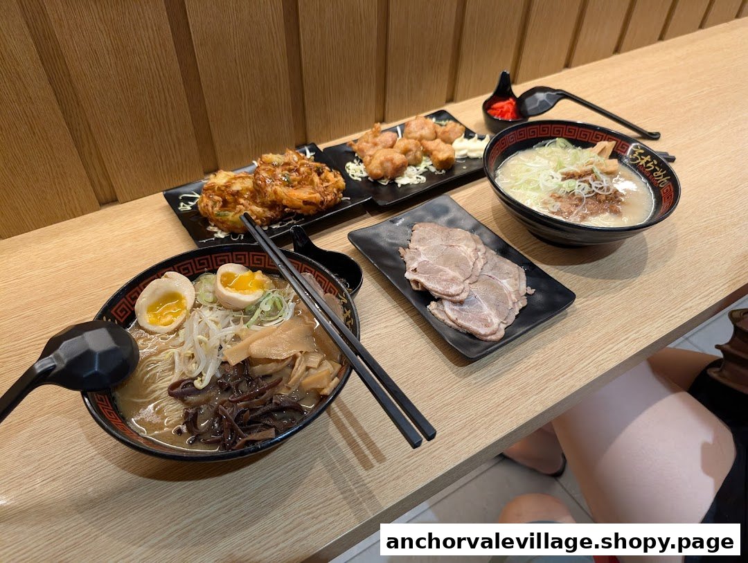 A table filled with two bowls of ramen, various side dishes, and sliced pork.