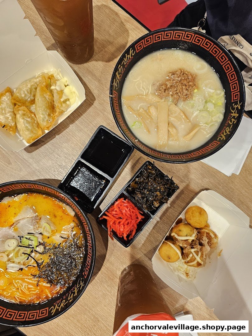 An overhead view of a table laden with two bowls of ramen, gyoza, takoyaki, and drinks.