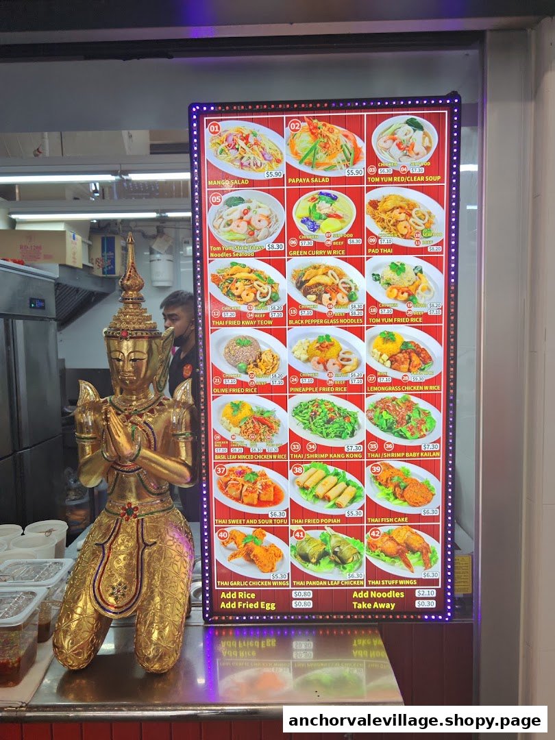 A golden Thai statue stands beside a brightly lit digital menu board displaying various Thai dishes and prices.