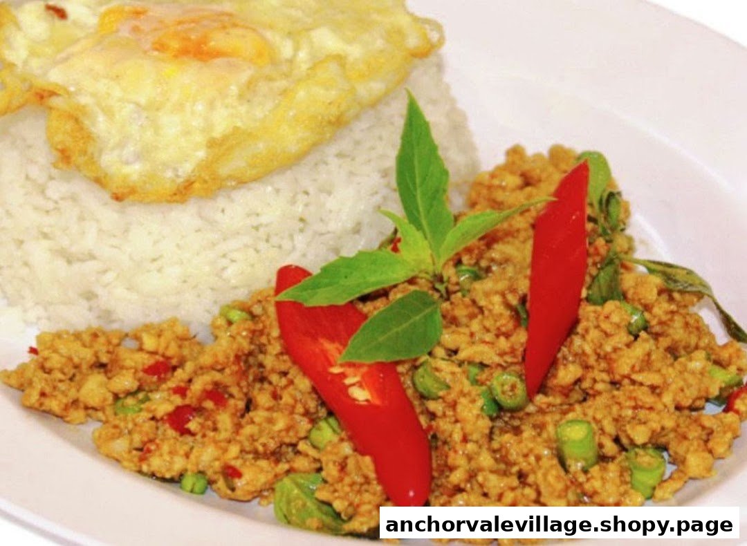 A vibrant plate of Thai stir-fried minced meat with rice, a fried egg, fresh basil, and red chilies.