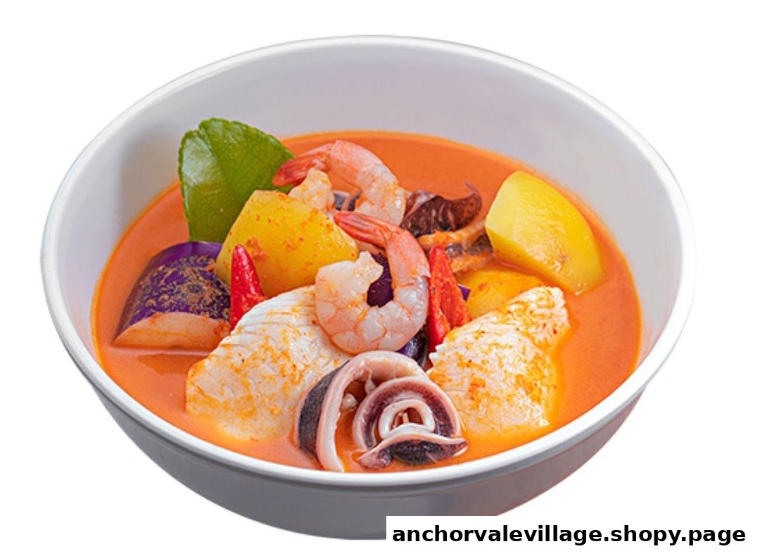 A vibrant bowl of Thai curry or soup with shrimp, squid, fish, potatoes, eggplant, and a kaffir lime leaf.