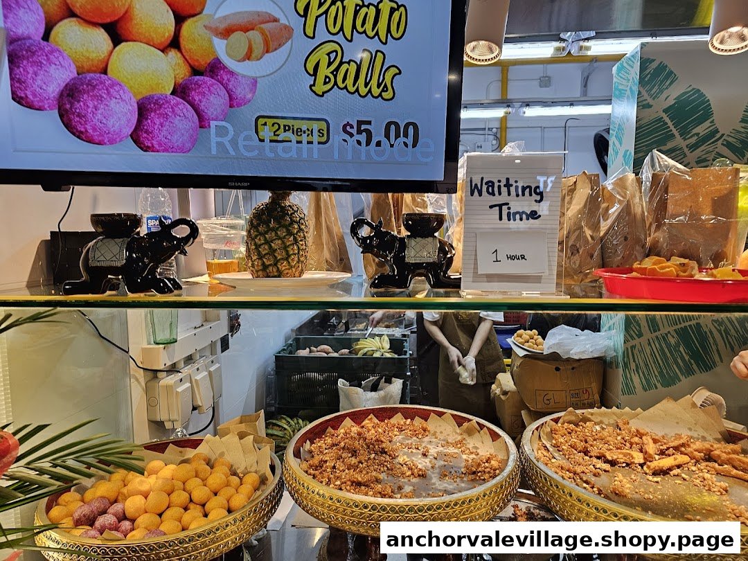 A vibrant display of Thai desserts and snacks, including sweet potato balls, at a bustling food stall.
