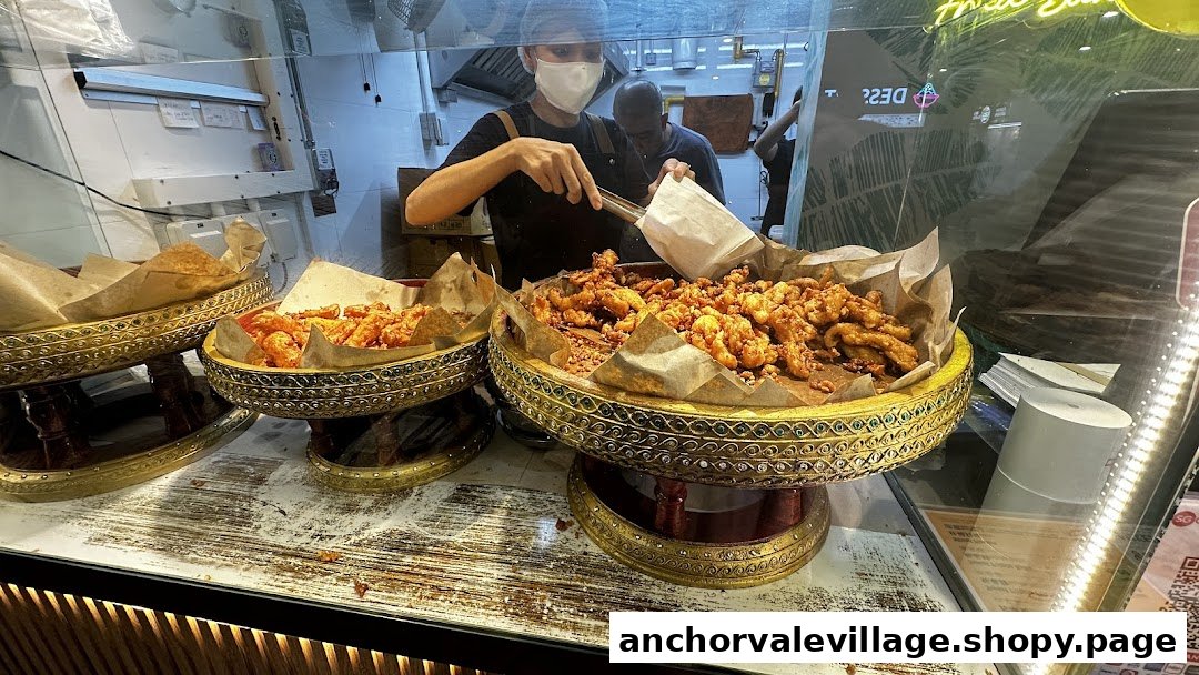 A staff member serving freshly fried Thai snacks from ornate display trays.