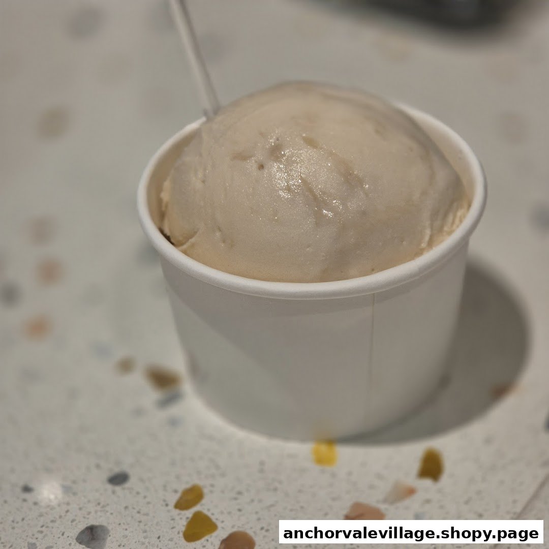 A single scoop of light-colored ice cream in a white paper cup on a speckled counter.