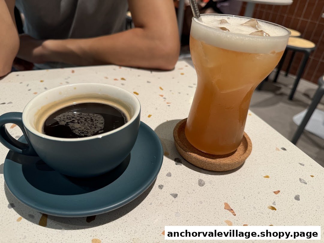 A close-up of a hot coffee and a cold beverage on a speckled white table.