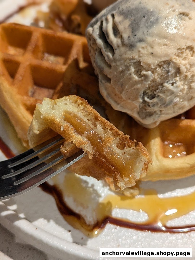 A close-up of a golden waffle with a scoop of ice cream, drizzled with syrup.