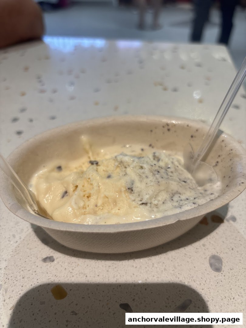 A bowl of creamy ice cream with two flavors and plastic spoons on a speckled counter.
