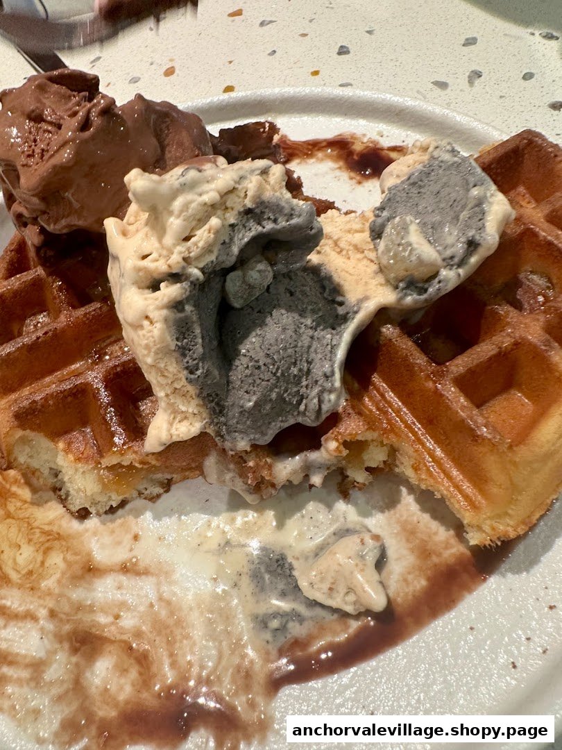 Waffles topped with multiple scoops of melting ice cream and chocolate sauce on a plate.
