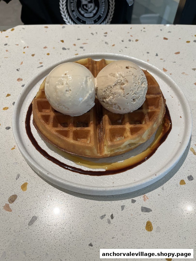 A delicious waffle topped with two scoops of ice cream and syrup on a speckled counter.