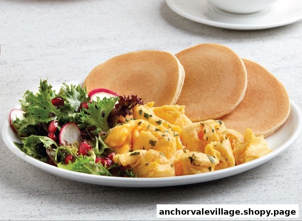 A plate featuring scrambled eggs, pancakes, and a fresh green salad with pomegranate and radish.