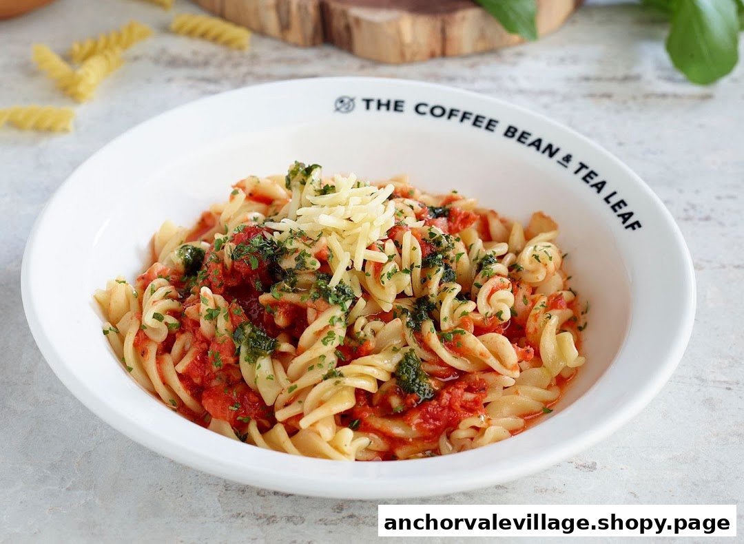 A white bowl filled with fusilli pasta, tomato sauce, herbs, and shredded cheese.