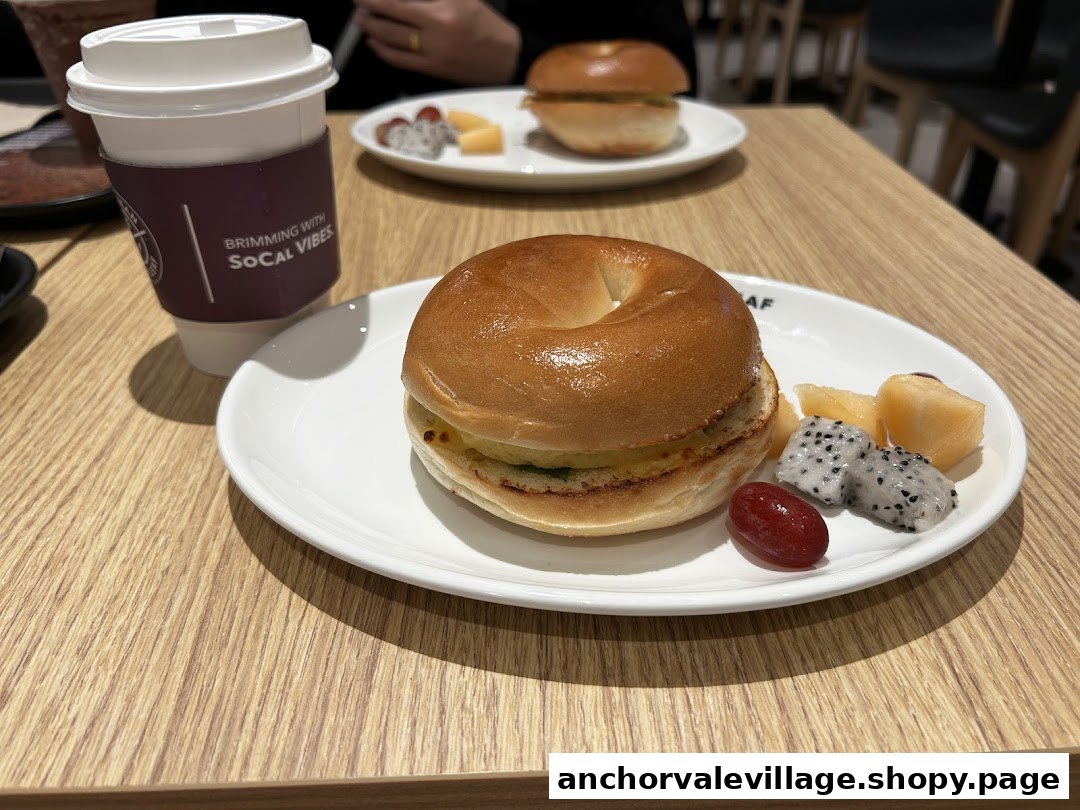 A bagel sandwich with a side of fresh fruit and a coffee cup on a wooden table.