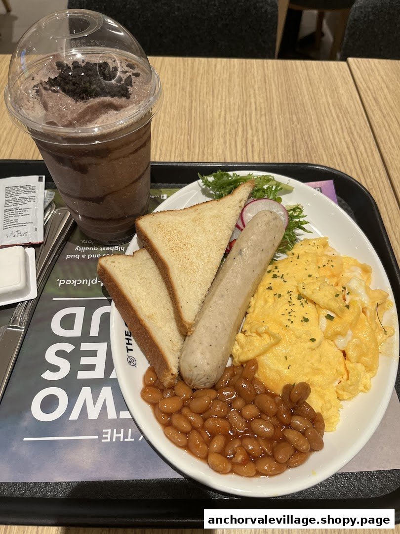 A hearty breakfast plate with scrambled eggs, sausage, baked beans, toast, and a chocolate blended drink.
