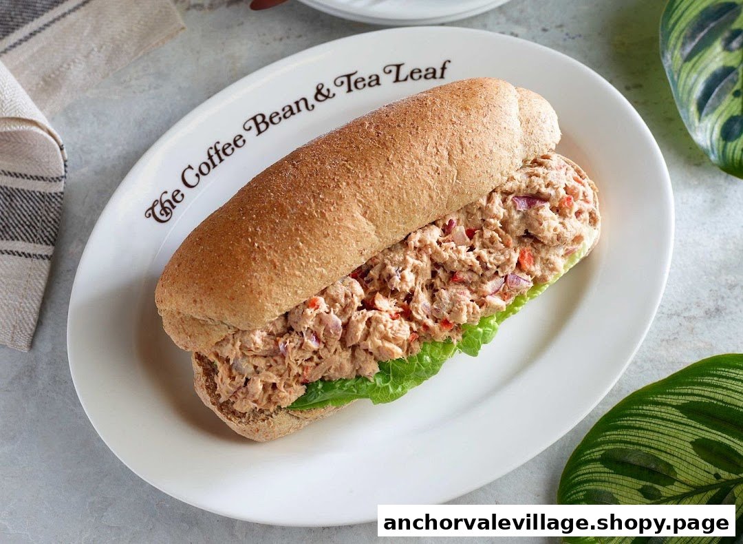 A tuna sandwich on a whole wheat bun with lettuce, served on a plate with the shop's logo.