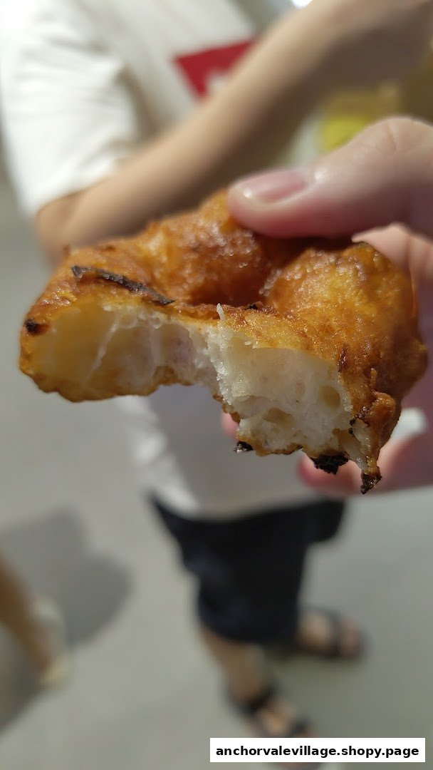A close-up of a hand holding a partially eaten, golden-brown vadai, showing its fluffy interior.