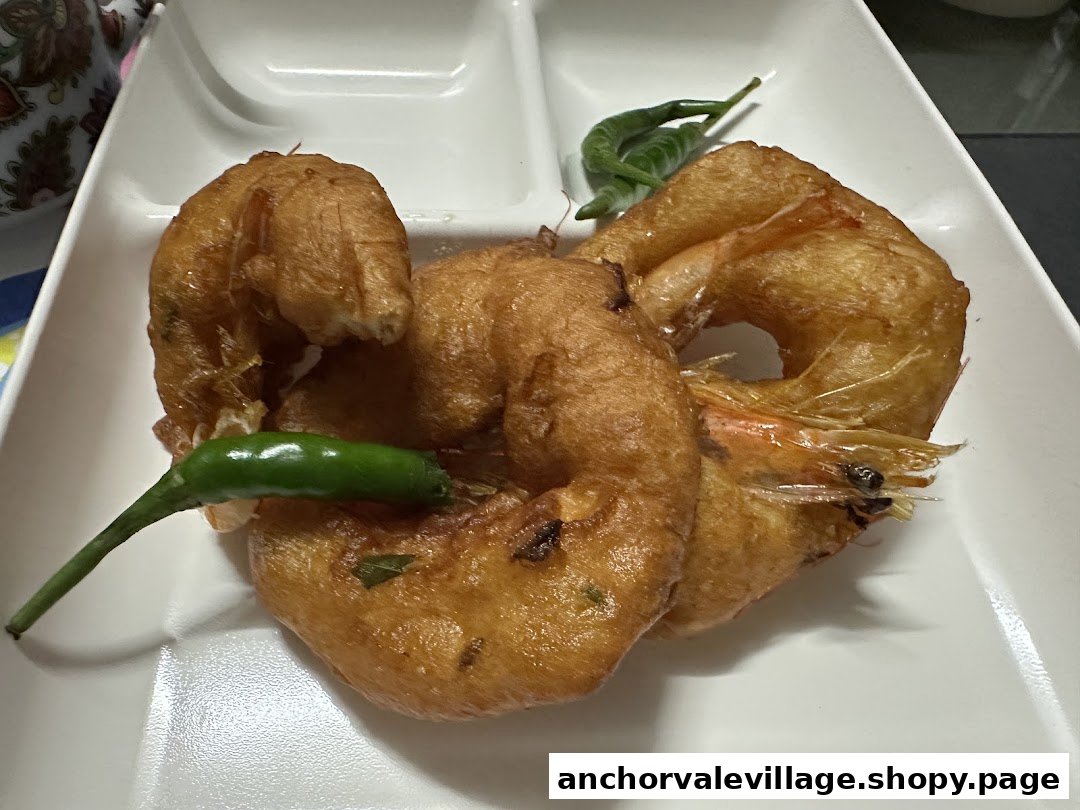 Close-up of golden-fried prawn vadai served with fresh green chilies on a white plate.
