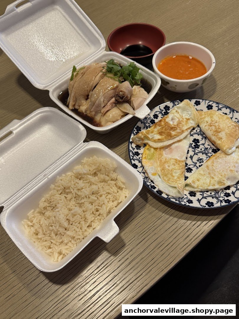 A delicious takeaway meal featuring Hainanese chicken rice, fried eggs, and dipping sauces on a wooden table.
