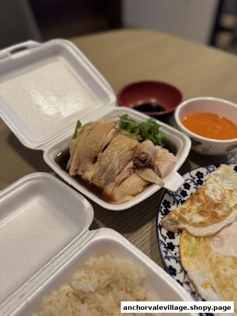 A delicious Hainanese chicken rice meal with fragrant rice, poached chicken, and fried eggs, served in takeout containers.