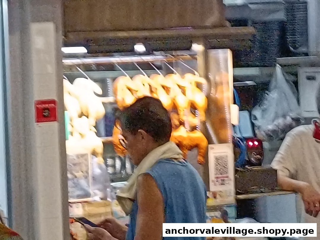 A person stands at a food stall counter displaying roasted chickens and ducks.