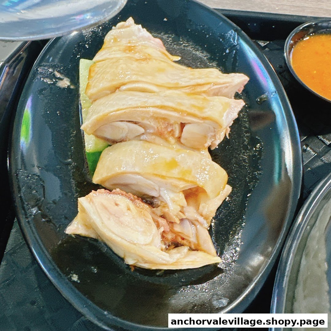 A close-up of tender, sliced Hainanese chicken served on a black plate with a side of chili sauce.