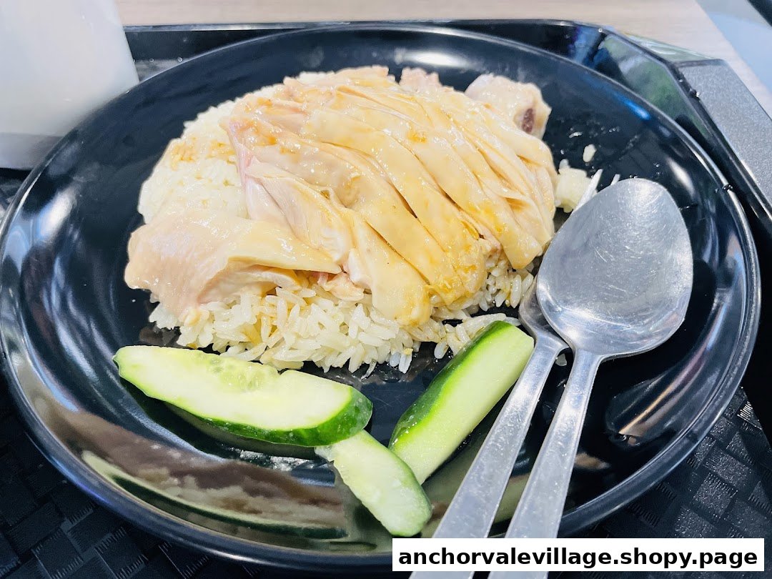 A close-up of a delicious plate of Hainanese chicken rice with cucumber slices on a black plate.