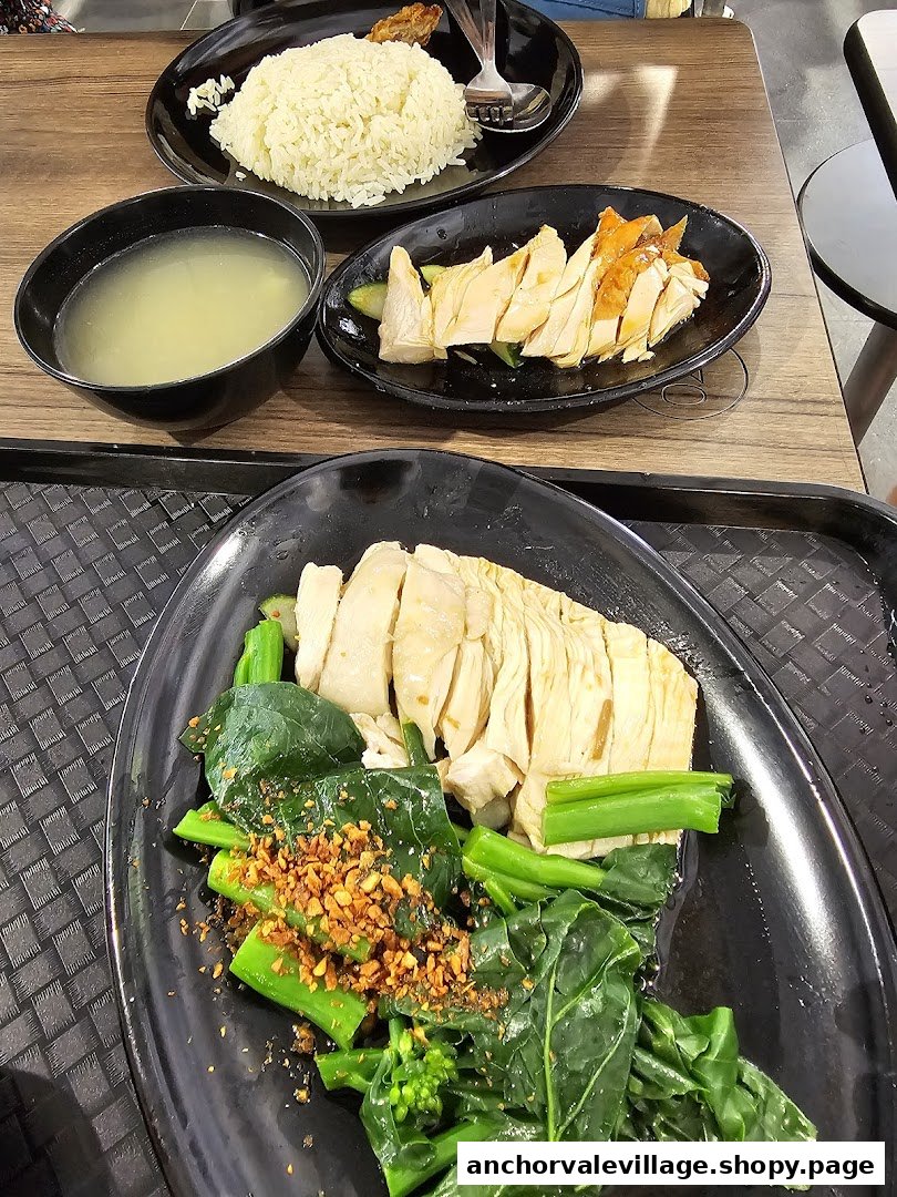 A delicious plate of chicken rice with steamed chicken, green vegetables, and a bowl of soup.