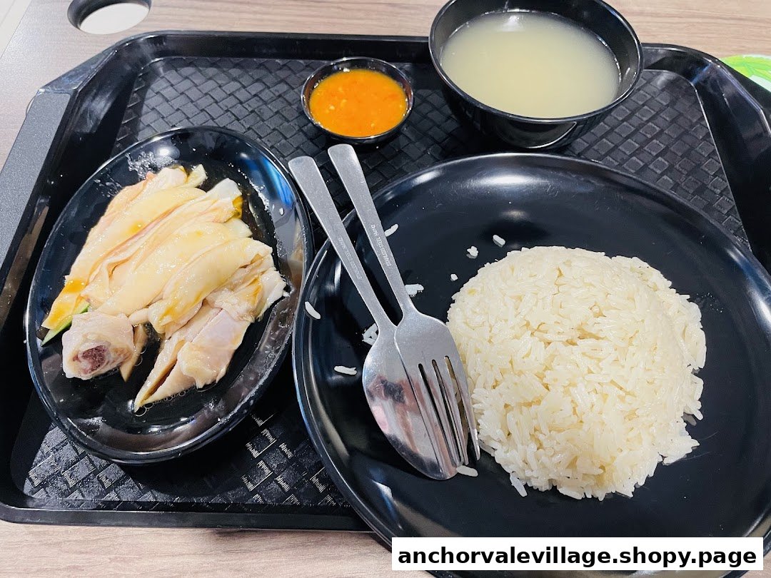 A delicious plate of Hainanese chicken rice with poached chicken, fragrant rice, soup, and chili sauce.