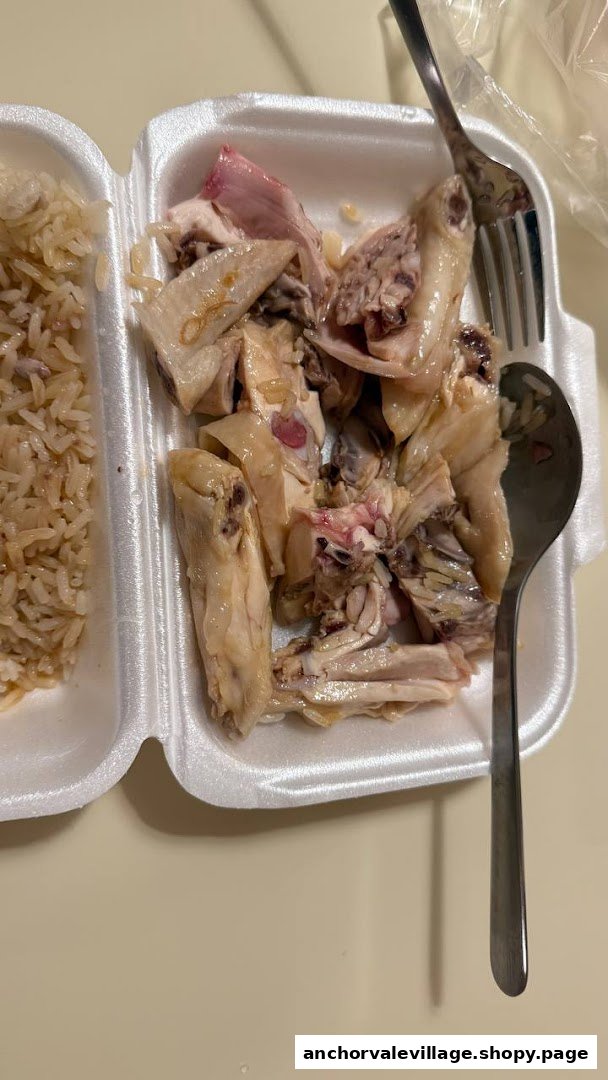 A close-up of chicken rice served in a white takeaway container with a fork and spoon.
