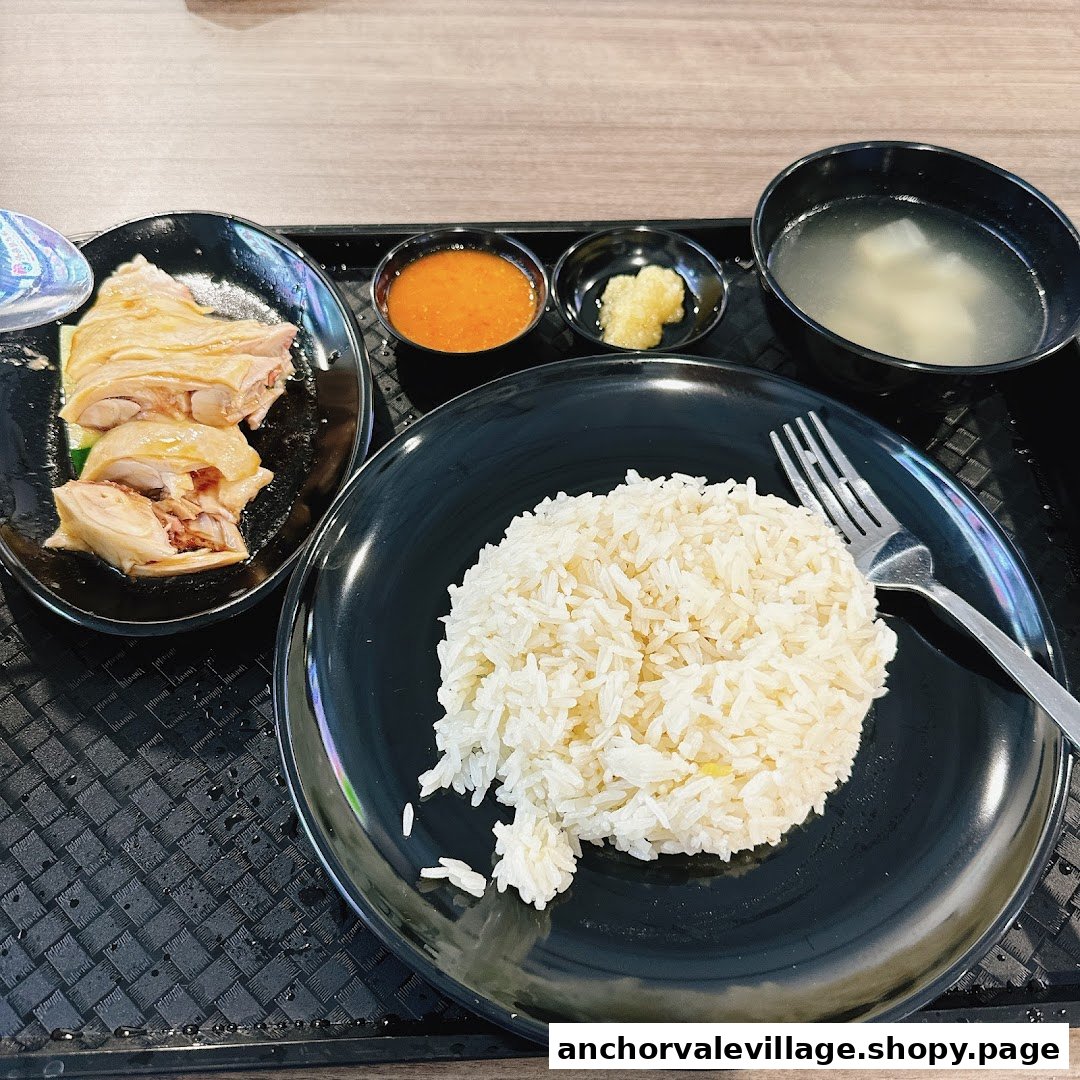 A classic Hainanese chicken rice meal featuring poached chicken, fragrant rice, soup, and chili sauce.