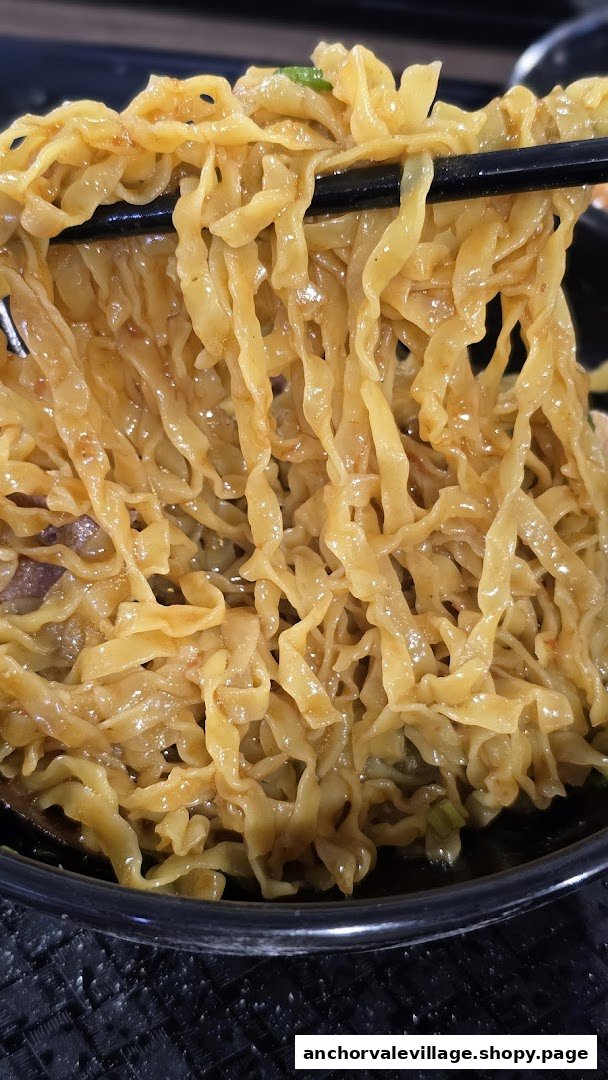 Close-up of delicious, saucy noodles being lifted from a bowl with chopsticks.
