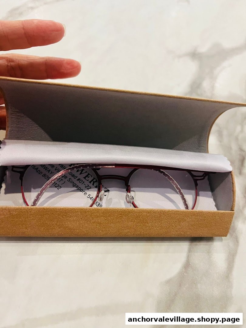 A pair of stylish red eyeglasses displayed in an open brown case with a white cleaning cloth.