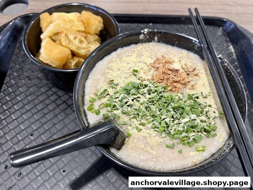 A comforting bowl of congee topped with spring onions, fried shallots, and a side of crispy fried dough.
