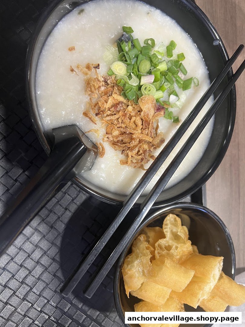 A bowl of congee with fried shallots and spring onions, served with fried dough.