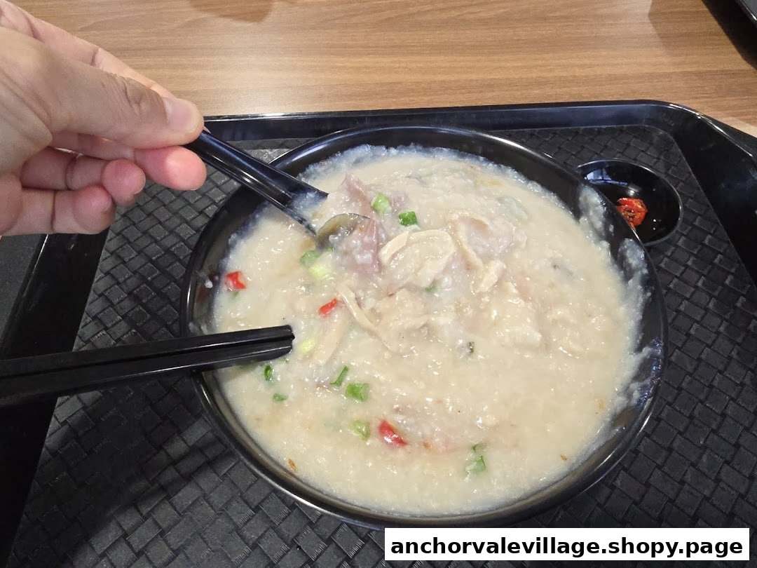 A close-up of a person eating a bowl of congee with various toppings and chili.