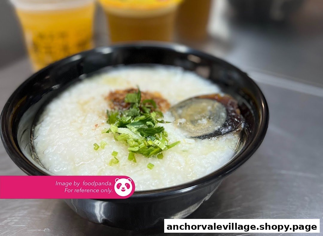 A close-up of a bowl of congee with century egg, garnished with spring onions and fried shallots.