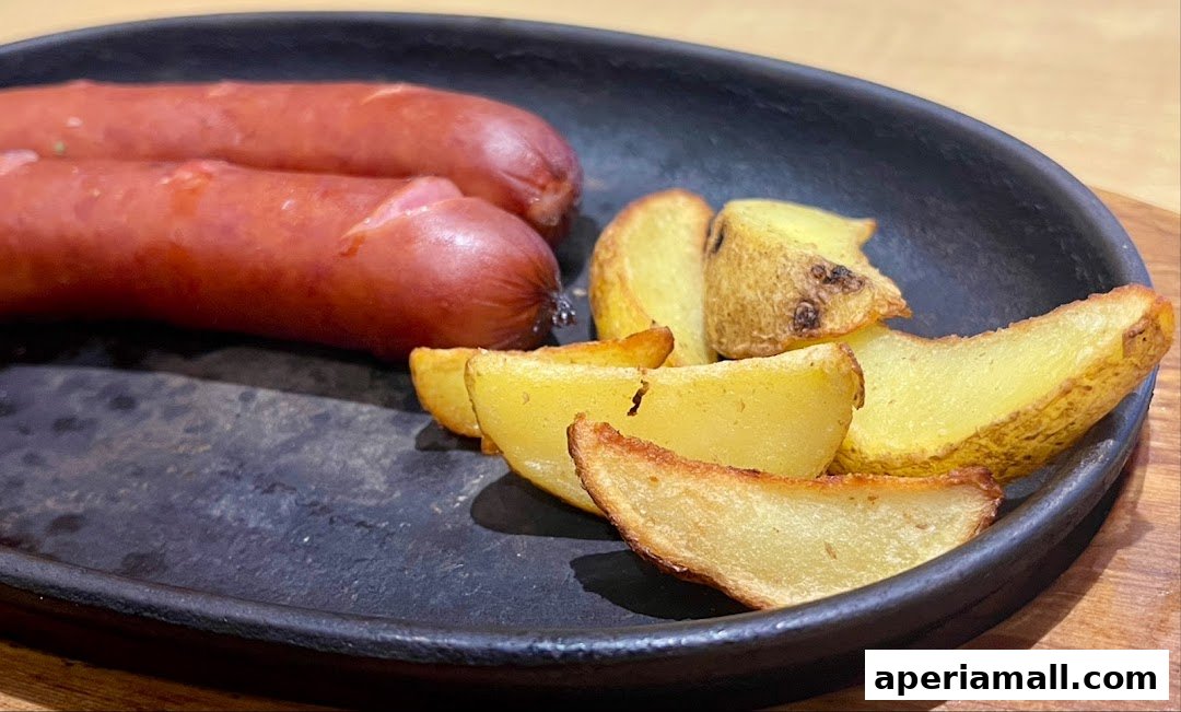 A close-up shot of two sausages and potato wedges served on a black plate.