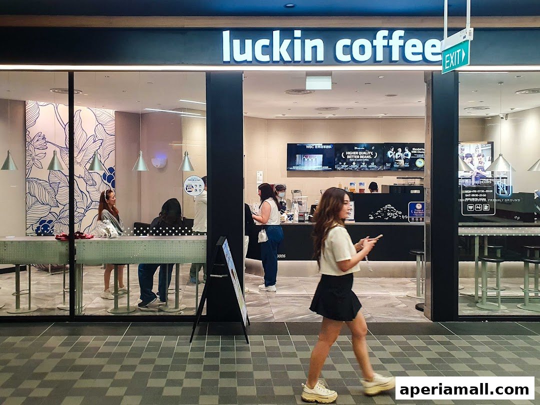 The exterior of a Luckin Coffee shop with customers inside and a person walking by.