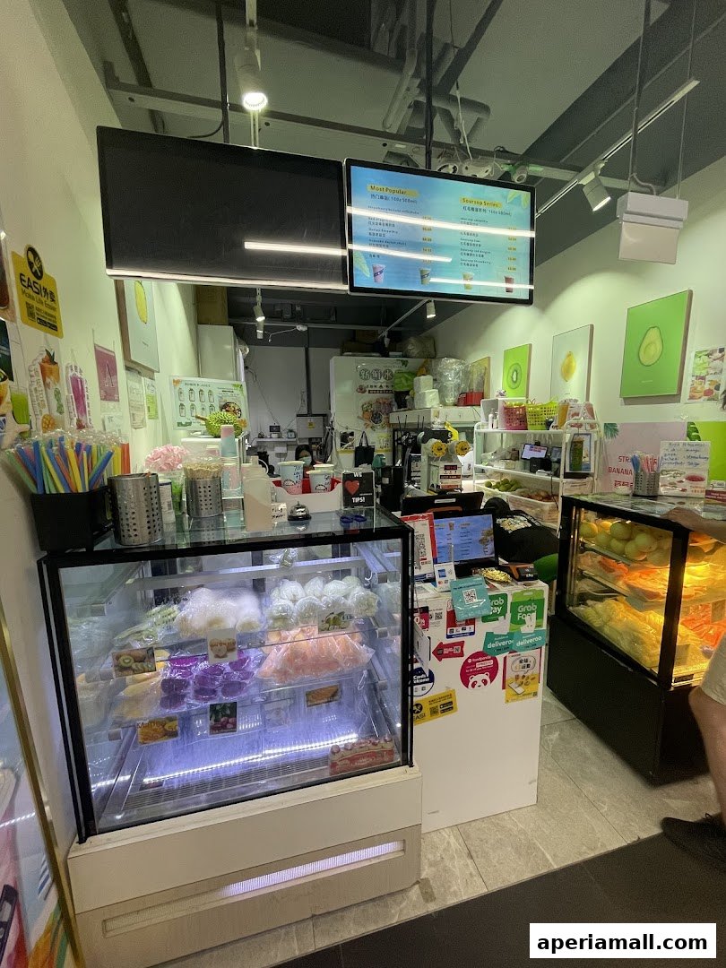A juice shop counter with a refrigerated display case filled with fruits and a digital menu board.