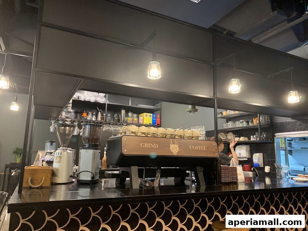 Interior shot of a coffee shop counter with espresso machine, grinders, and shelves of cups.