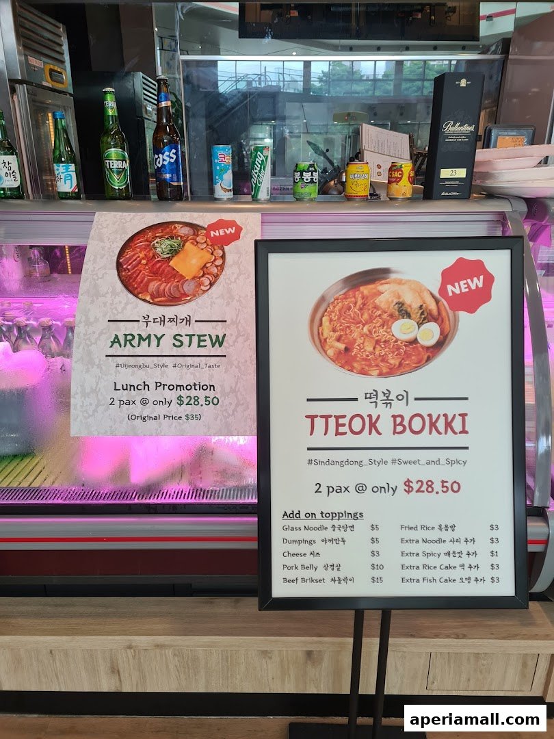 A display showcasing Korean dishes, Army Stew and Tteokbokki, with promotional pricing and add-on options.