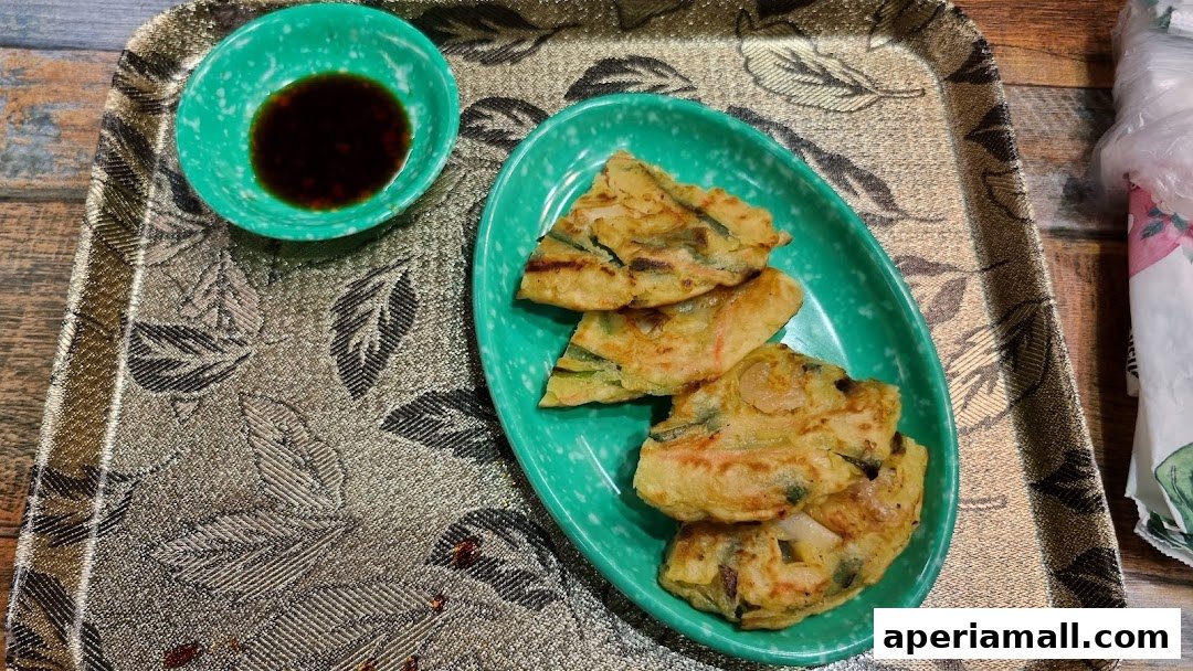 A close-up of Korean savory pancakes (jeon) served with a dipping sauce on a decorative tray.