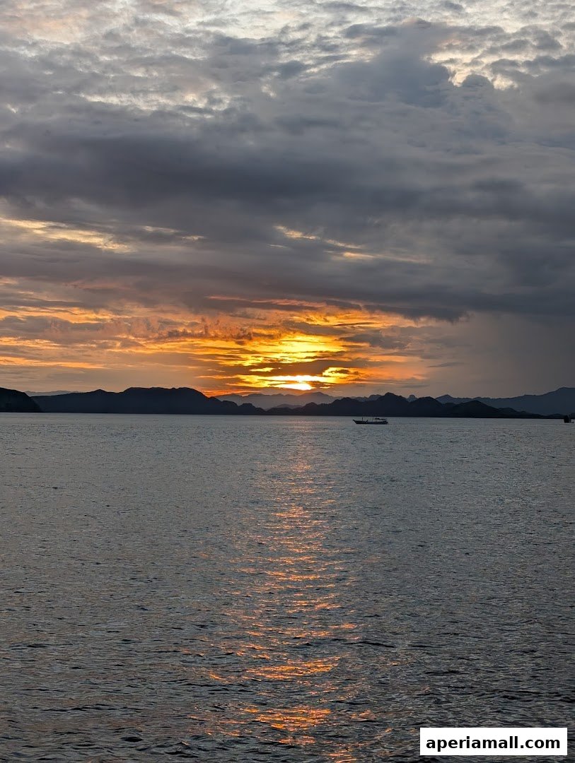 A serene sunset over the ocean with a boat sailing in the distance.