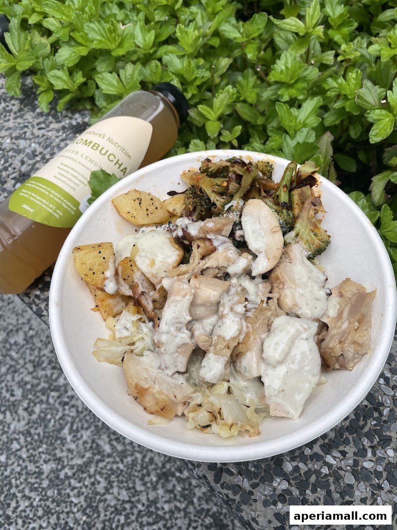 A bowl of salad with chicken and roasted vegetables, next to a bottle of kombucha.