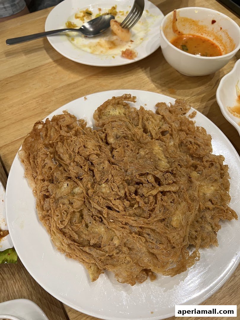 A close-up of a crispy Thai omelet served on a white plate with a side of dipping sauce.