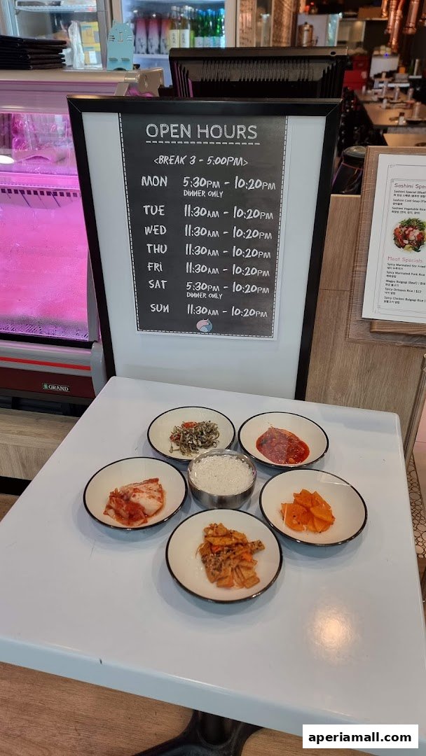 A table with Korean side dishes and rice, next to an open hours sign.