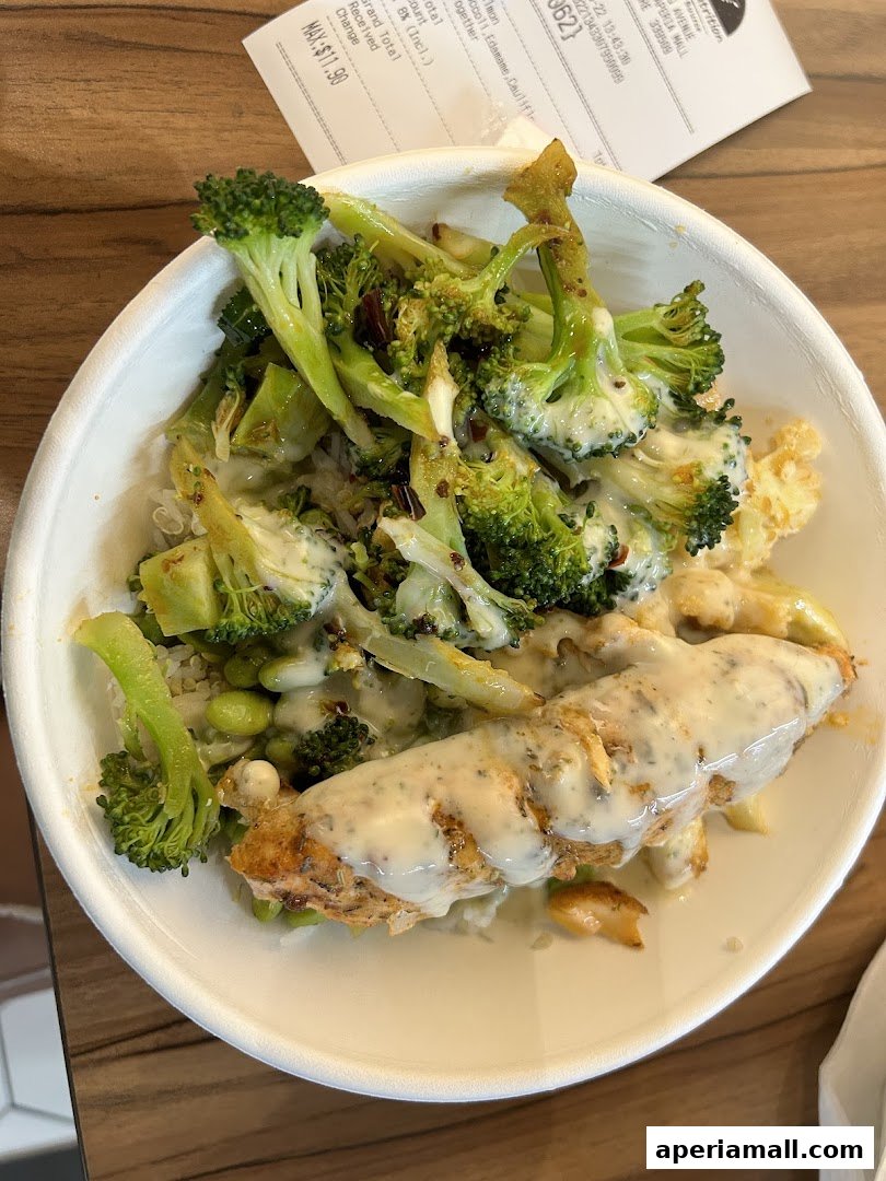 A healthy bowl of salmon, broccoli, edamame, and cauliflower with a creamy sauce.